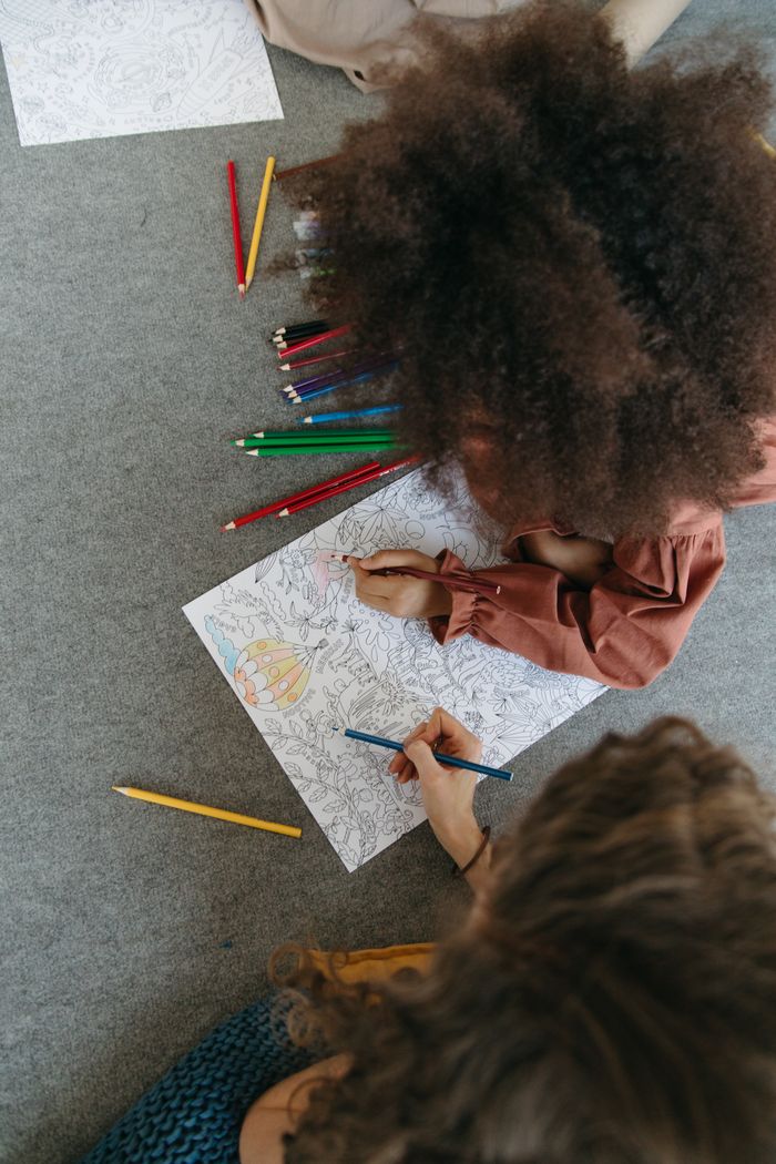 Top view of two children drawing with colored pencils on paper, engaging in a creative hobby.